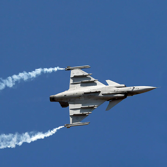 A fighter jet leaves behind two smoke trails as it flies in a blue sky